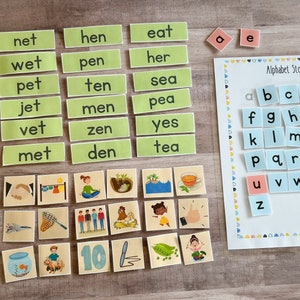 May include: A set of colorful alphabet tiles with the letters a through z, along with a set of green word tiles with words like "wed", "net", "hen", "eat", "red", "wet", "pen", "her", "fed", "pet", "ten", "sea", "bed", "jet", "men", "pea", "led", "vet", "zen", "yes", "met", "den", and "tea". There are also several small picture cards with various images.