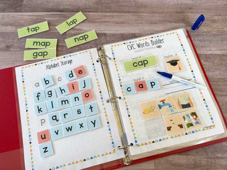 May include: A binder with a white page open to a CVC words builder activity. The page has the word "cap" written on it and a picture of a graduation cap. There are also letter tiles for the alphabet and a blue dry-erase marker.