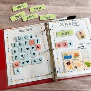 May include: A red binder with a clear plastic cover. The left side of the binder has a page with the title "Alphabet Storage" and a grid of colorful letter tiles. The right side of the binder has a page with the title "CVC Words Builder" and a section for building words with letter tiles. The page also includes a picture of a girl eating a pea pod.