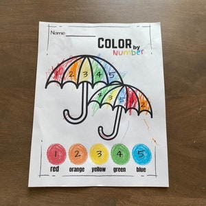 May include: Color by number activity sheet featuring two umbrellas with rainbow colors. The numbers 1 through 5 are written on the umbrellas, and the corresponding colors are shown below: red, orange, yellow, green, and blue.