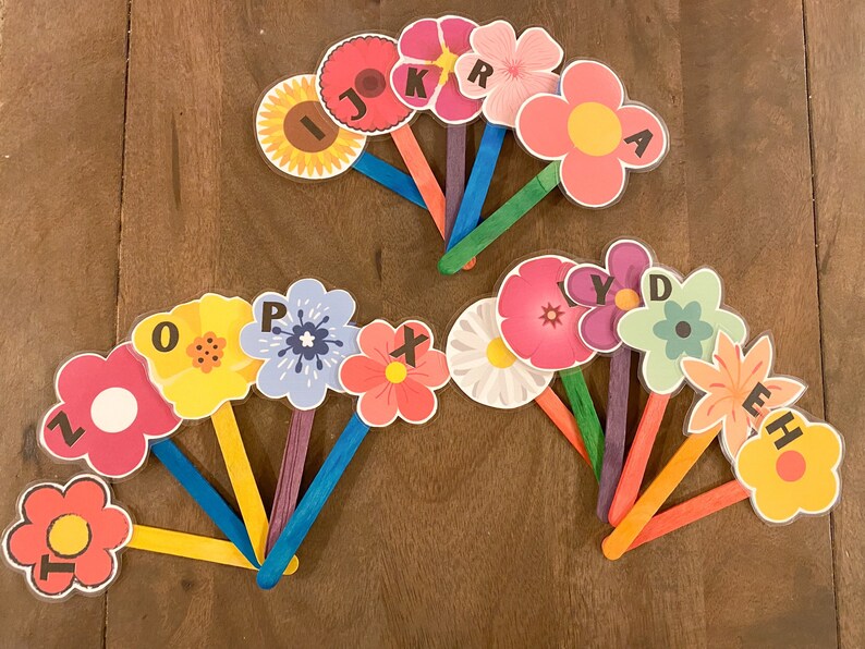 K&ouml;nnte beinhalten: Ein Satz von 14 bunten, blumenf&ouml;rmigen Karten mit darauf gedruckten Buchstaben des Alphabets. Die Karten sind an Holzst&auml;bchen befestigt.