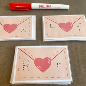 Op de afbeelding: Drie stapels kaarten met een roze envelopontwerp. Elke kaart heeft een hart en een letter in de envelop. De letters zijn X, F en R.