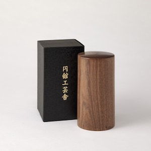 May include: A wooden cylindrical container with a black box. The box has Japanese text that reads "円筒 工芸 会".