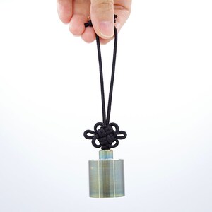 K&ouml;nnte beinhalten: Ein silberner Metallzylinder mit einem schwarzen Band, das zu einem Knoten gebunden ist, h&auml;ngt an einer Hand. Der Zylinder hat eine strukturierte Oberfl&auml;che.