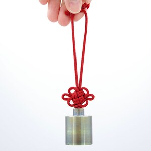 K&ouml;nnte beinhalten: Ein silbernes zylindrisches Gewicht mit einer daran befestigten roten Schnur. Der Knoten ist ein traditioneller chinesischer Gl&uuml;cksknoten.