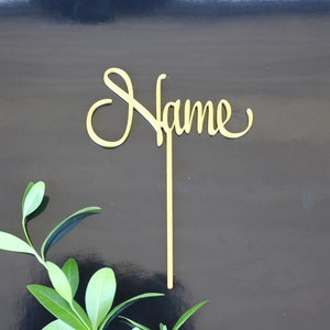 May include: Gold-coloured wooden sign with the word "Name" written in a cursive font. The sign is attached to a wooden stick.