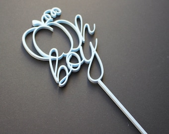 May include: Light blue cake topper with the words "Oh Boy" in a cursive font. The topper is designed to be placed on a cake for a baby shower or birthday celebration.