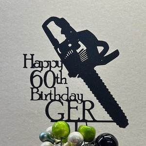 May include: Black metal silhouette of a chainsaw with the text "Happy 60th Birthday GER" on a brown pot with green and black decorative balls.