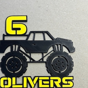 Può includere: Topper per torta a forma di monster truck nero con un numero 6 giallo sul tetto e il nome "OLIVERS" in lettere gialle.