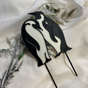 May include: Black and white penguin cake topper featuring two penguins standing together. The penguins are made of plastic and have a glossy finish.