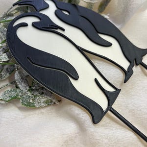 May include: Black and white 3D printed penguin cake topper. The penguins are standing side by side with their heads touching.