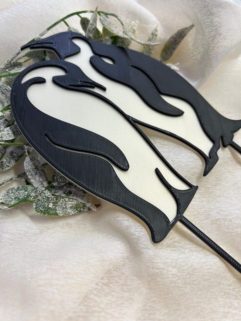 May include: Black and white 3D printed penguin cake topper. The penguins are standing side by side with their heads touching.