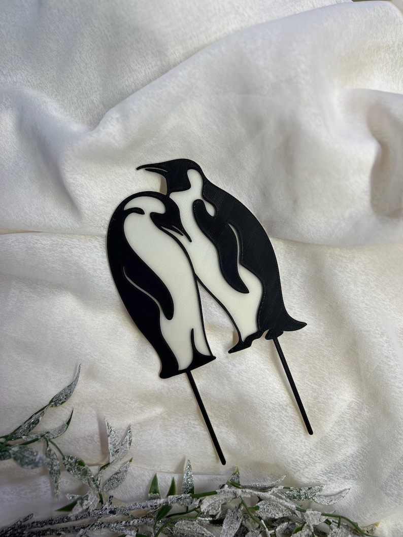 May include: Two black and white penguin silhouettes on sticks, facing each other. The penguins are in a romantic pose, with their heads tilted towards each other.