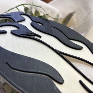 May include: A black and white 3D printed wall decoration with a wavy design. The design is reminiscent of a stylised flame or wave.