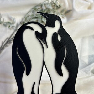 May include: A black and white 3D printed penguin couple figurine. The penguins are standing close together, with their heads touching. The figurine is a romantic and whimsical decoration for a home or office.