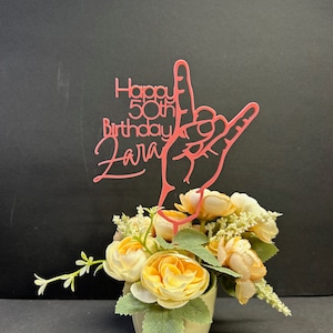 Może przedstawiać: Różowy akrylowy topper na tort z tekstem "Happy 50th Birthday Zara" i ręką wykonującą znak "Kocham Cię". Topper umieszczony jest w białej ceramicznej doniczce z bukietem żółtych i białych kwiatów.