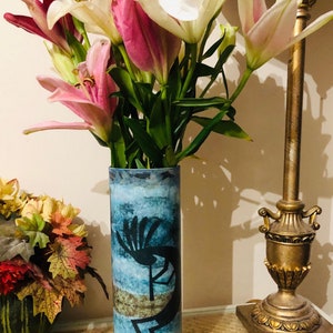 May include: A blue and brown ceramic vase with a Native American design. The vase is filled with white and pink lilies.