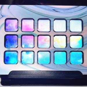 May include: A white and blue marbled surface with 16 square compartments. Each compartment has a different color of blue, pink, and white. The surface is on a black stand.