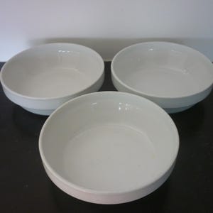 Può includere: Tre ciotole in ceramica bianca di diverse dimensioni. Le ciotole sono rotonde e hanno una finitura liscia e lucida.