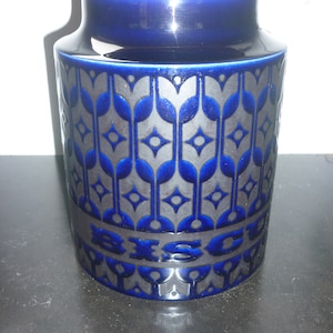 May include: A blue ceramic biscuit jar with a wooden lid and a geometric pattern in silver. The word "BISCUIT" is written in silver on the front of the jar.