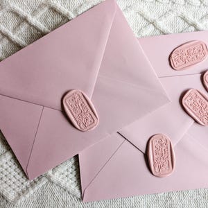 Può includere: Due buste rosa con sigilli di cera decorativi. I sigilli sono di forma rettangolare e presentano un motivo floreale.