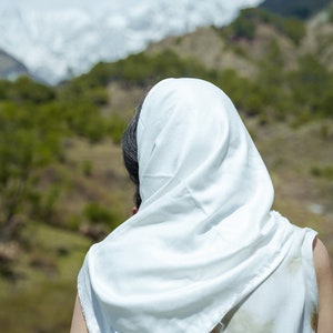 Puede incluir: Una persona con un pa&ntilde;uelo blanco en la cabeza se encuentra de espaldas a la c&aacute;mara, mirando hacia una cordillera en la distancia.