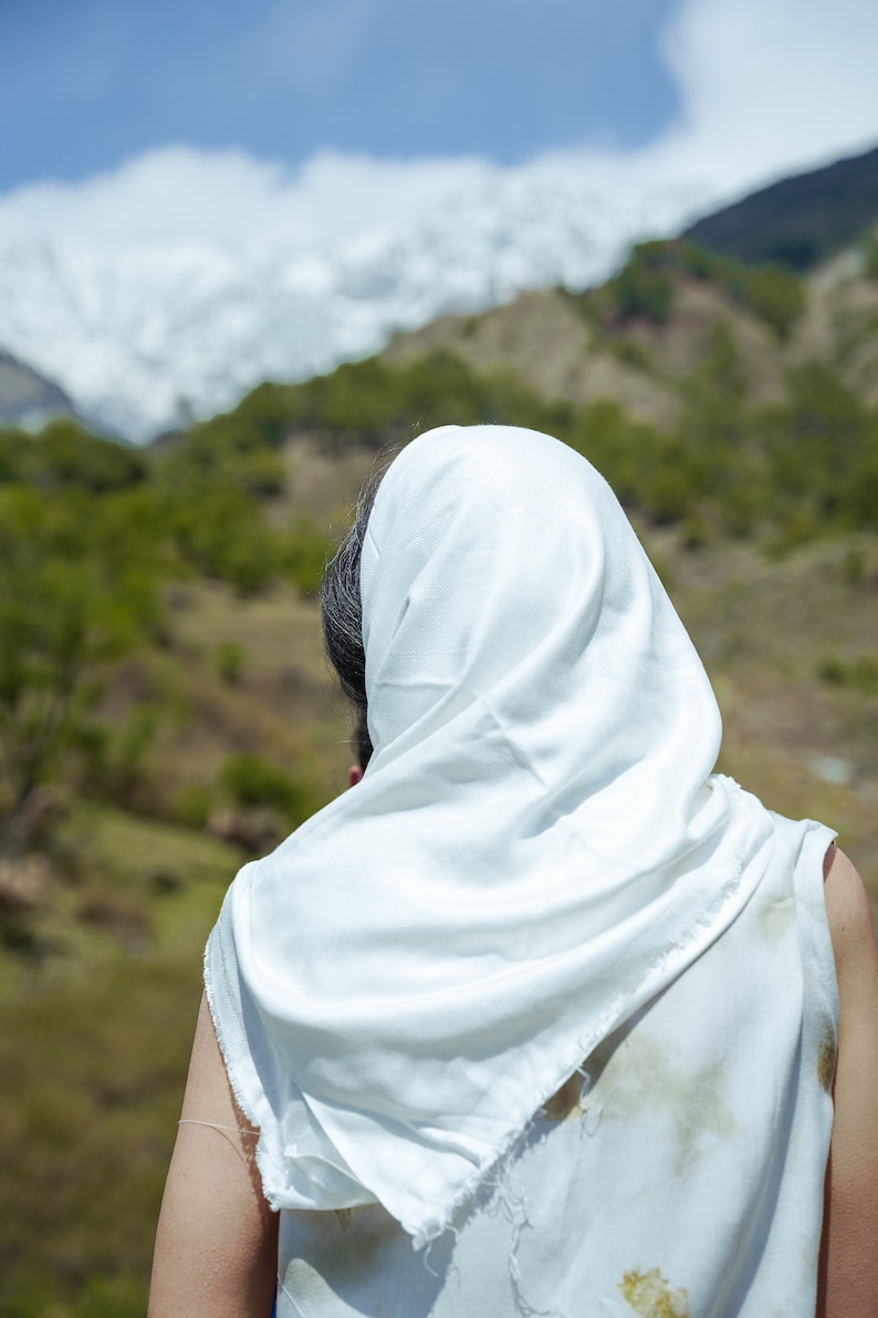 Puede incluir: Una persona con un pa&ntilde;uelo blanco en la cabeza se encuentra de espaldas a la c&aacute;mara, mirando hacia una cordillera en la distancia.