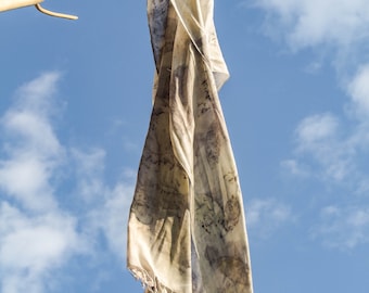 May include: A white silk scarf with brown and grey patterns hangs from a branch against a blue sky with white clouds.