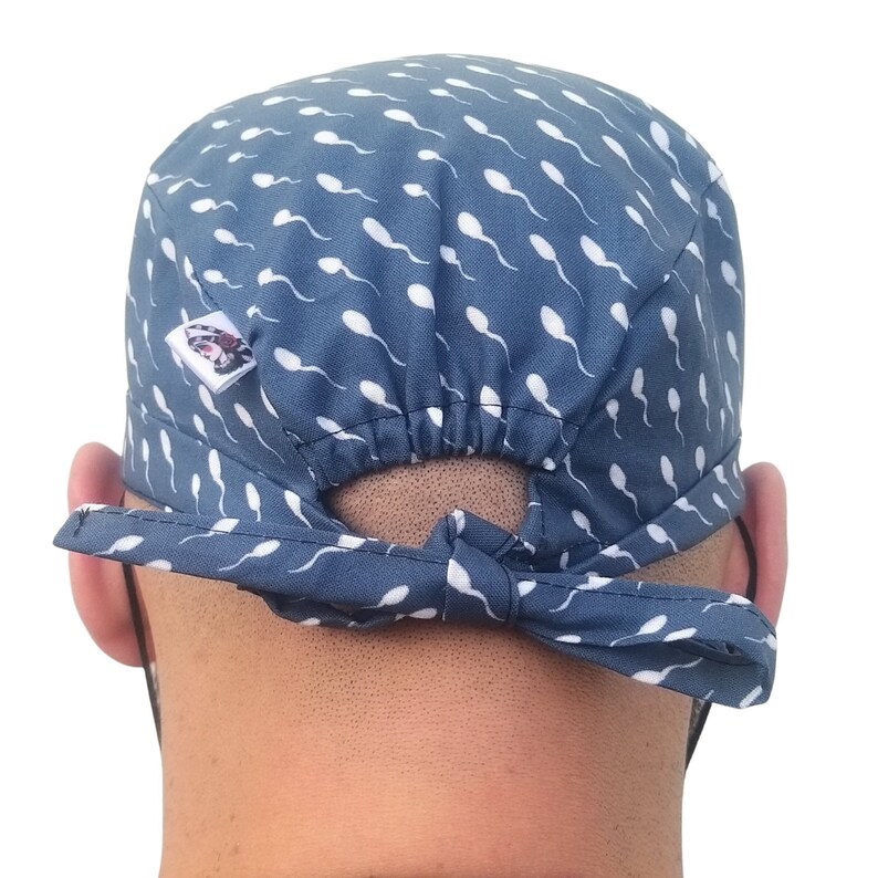 May include: A blue and white patterned surgical scrub hat with a white elastic band. The hat has a white sperm-shaped pattern.