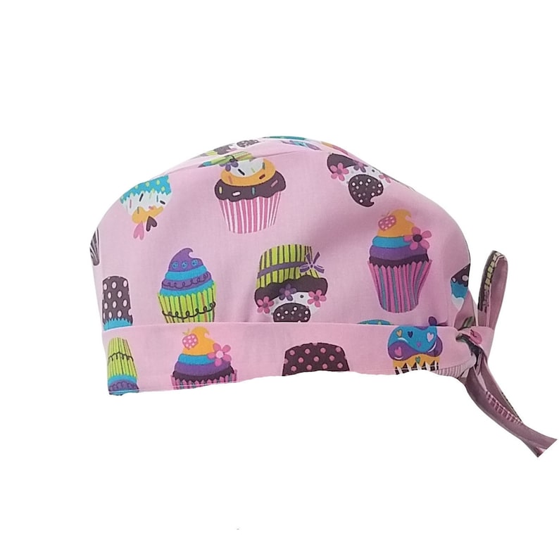 May include: Pink surgical scrub hat with a cupcake pattern. The hat has a tie on the back.