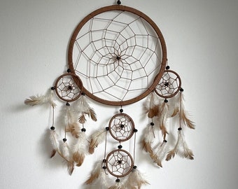 May include: A brown dreamcatcher with feathers hanging from the bottom. The dreamcatcher has a large circle in the center and two smaller circles below it.