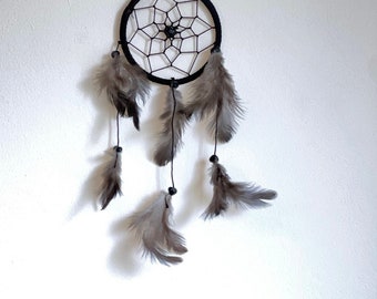May include: A black dreamcatcher with a web-like design and gray feathers hanging from it.