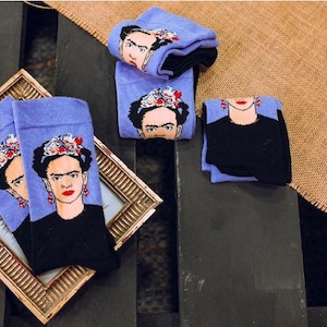 Könnte beinhalten: Vier Paar violette und schwarze Socken mit einem aufgedruckten Bild von Frida Kahlo.