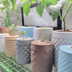 May include: A close-up of a set of nine round, textured, white, gray, brown, and blue planters with small plants growing in them. The planters are arranged in a row on a green metal shelf.