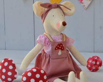 May include: A stuffed fabric mouse toy with cream-colored skin, wearing a pink polka-dot blouse and a dusty rose skirt with a red and white mushroom patch. The mouse has a matching dusty rose headband and is surrounded by red and white polka-dot mushrooms.