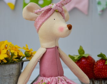 Könnte beinhalten: Handgefertigte Stoffmaus-Puppe mit einem rosa Kleid mit geblümtem Rock und passendem gepunkteten Stirnband. Die Puppe hat einen hellbeige Körper, rosa Wangen und eine braune Nase. Gelbe Blumen und Erdbeeren sind im Hintergrund.