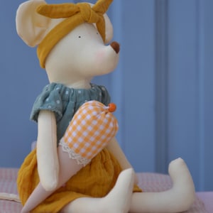 K&ouml;nnte beinhalten: Eine handgefertigte Pl&uuml;schmauspuppe mit gelbem Stirnband und gr&uuml;nem Polka-Dot-Kleid. Die Puppe h&auml;lt ein kegelf&ouml;rmiges Spielzeug mit einem orange-wei&szlig; karierten Muster. Der Rock der Puppe ist gelb und das Spielzeug hat eine Spitzenborte.