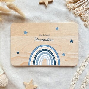 May include: A wooden sign with a blue and white rainbow design and stars. The sign says "Hier kr&uuml;melt Maximilian".