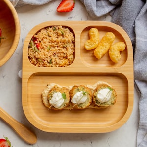 Peut inclure: Une assiette divis&eacute;e en bois avec quatre sections. La section sup&eacute;rieure gauche contient une portion de couscous avec des l&eacute;gumes. La section sup&eacute;rieure droite contient quelques en-cas de fromage souffl&eacute;. La section inf&eacute;rieure contient trois aliments pan&eacute;s et frits avec une cuiller&eacute;e de sauce blanche sur le dessus.