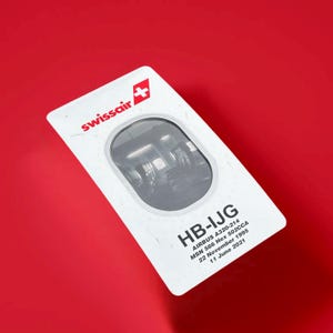 May include: A white card with the Swissair logo and the text "HB-IJG" in black. The card also includes the text "AIRBUS A320-214", "MSN 566 Hex 502CCA", "22 November 1995", and "11 June 2021".