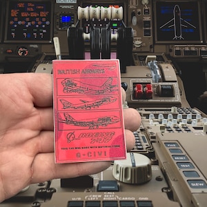 May include: A red tag with a white outline featuring a British Airways Boeing 747 aeroplane. The tag reads "British Airways Boeing 747 This tag was made with material from G-CIVI".