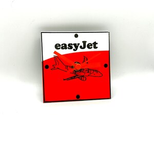 May include: A red and white square clock with a black and white airplane graphic and the text "easyJet" in black. The clock hands are orange.
