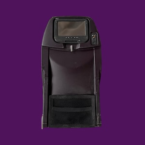 May include: A dark brown airplane seat back with a small screen, control panel, and a mesh pocket. The screen is rectangular and has a dark border. The seat back is against a purple background.