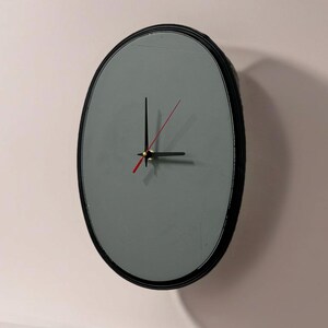 May include: A gray oval clock with black hands and a black frame. The clock is set to 10:10.