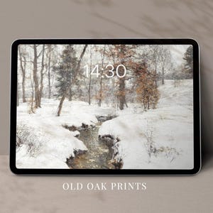 Op de afbeelding: Een digitale tablet met een winterscène met een beek die door een besneeuwd bos stroomt. De tijd is 14:30. De tekst "Old Oak Prints" wordt onder de tablet weergegeven.