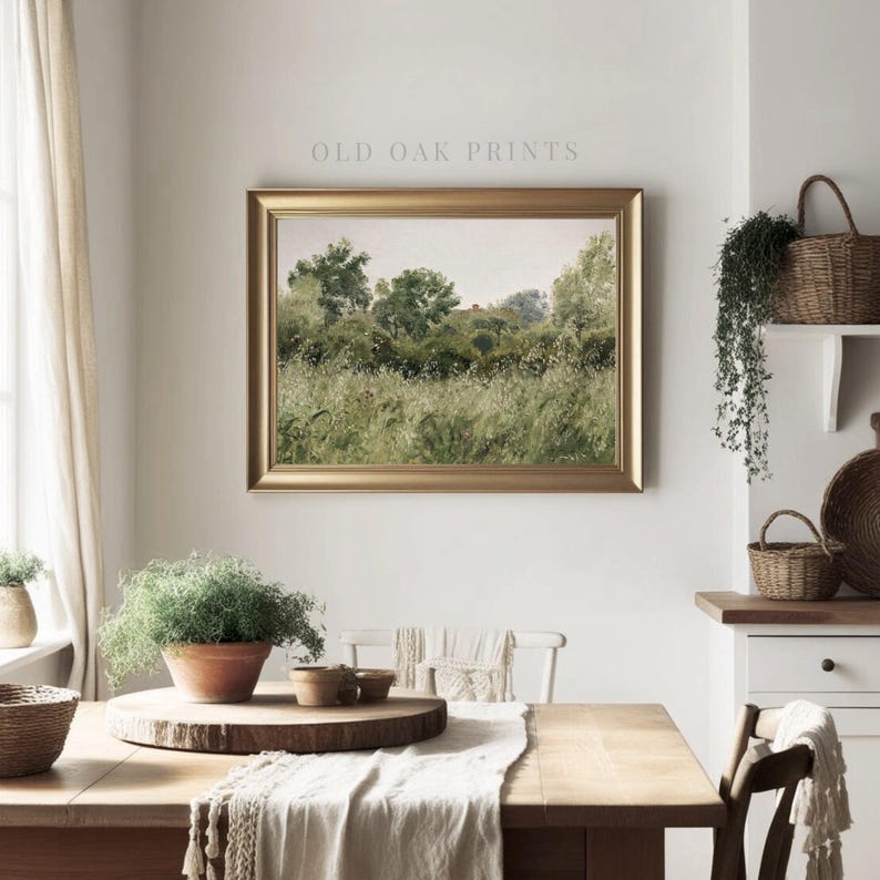 May include: A framed print of a watercolour painting depicting a lush green field with a small red house in the distance. The print is hanging on a white wall in a room with a wooden table and chairs.