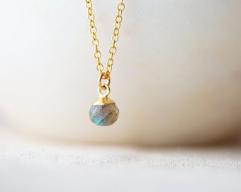 May include: A gold chain necklace with a single, round, iridescent labradorite gemstone pendant.
