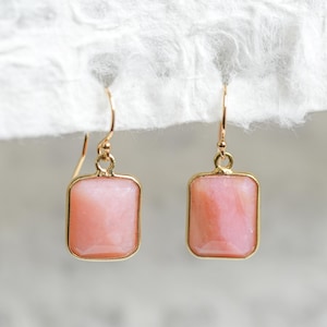 May include: A pair of gold earrings with pink opal stones set in a square shape.