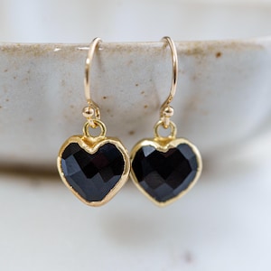 May include: A pair of gold heart-shaped earrings with black gemstone accents.