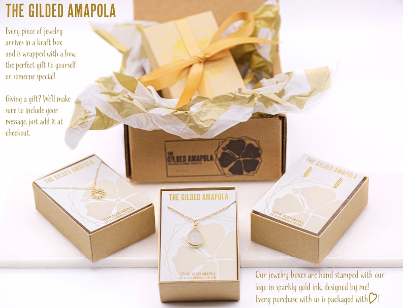 May include: A product shot of jewelry boxes from The Gilded Amapola. The boxes are kraft-colored with gold accents and a gold ribbon. The boxes contain necklaces and earrings. Text on the boxes reads "THE GILDED AMAPOLA".